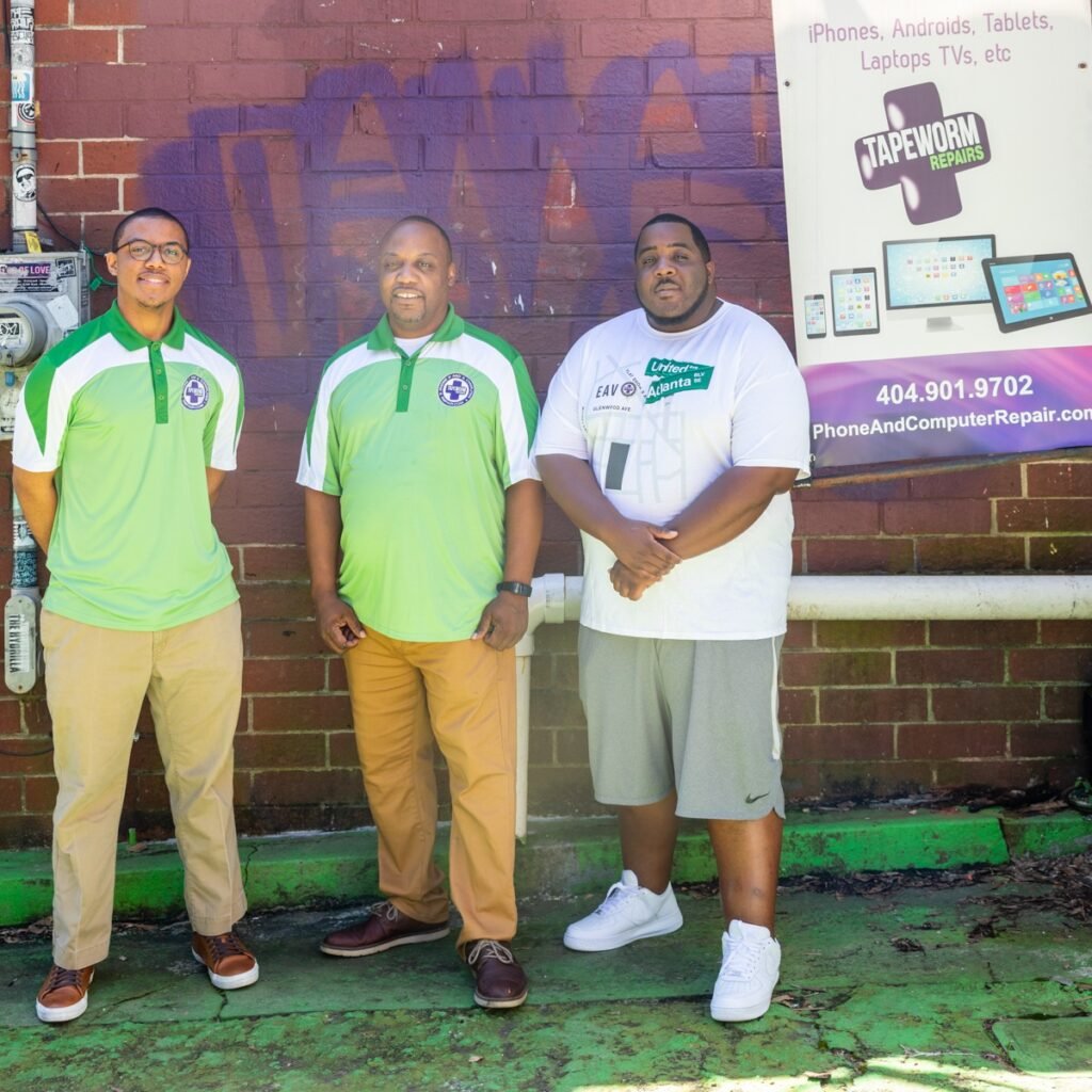 Tapeworm Repairs team outside the shop with purple and green business signage